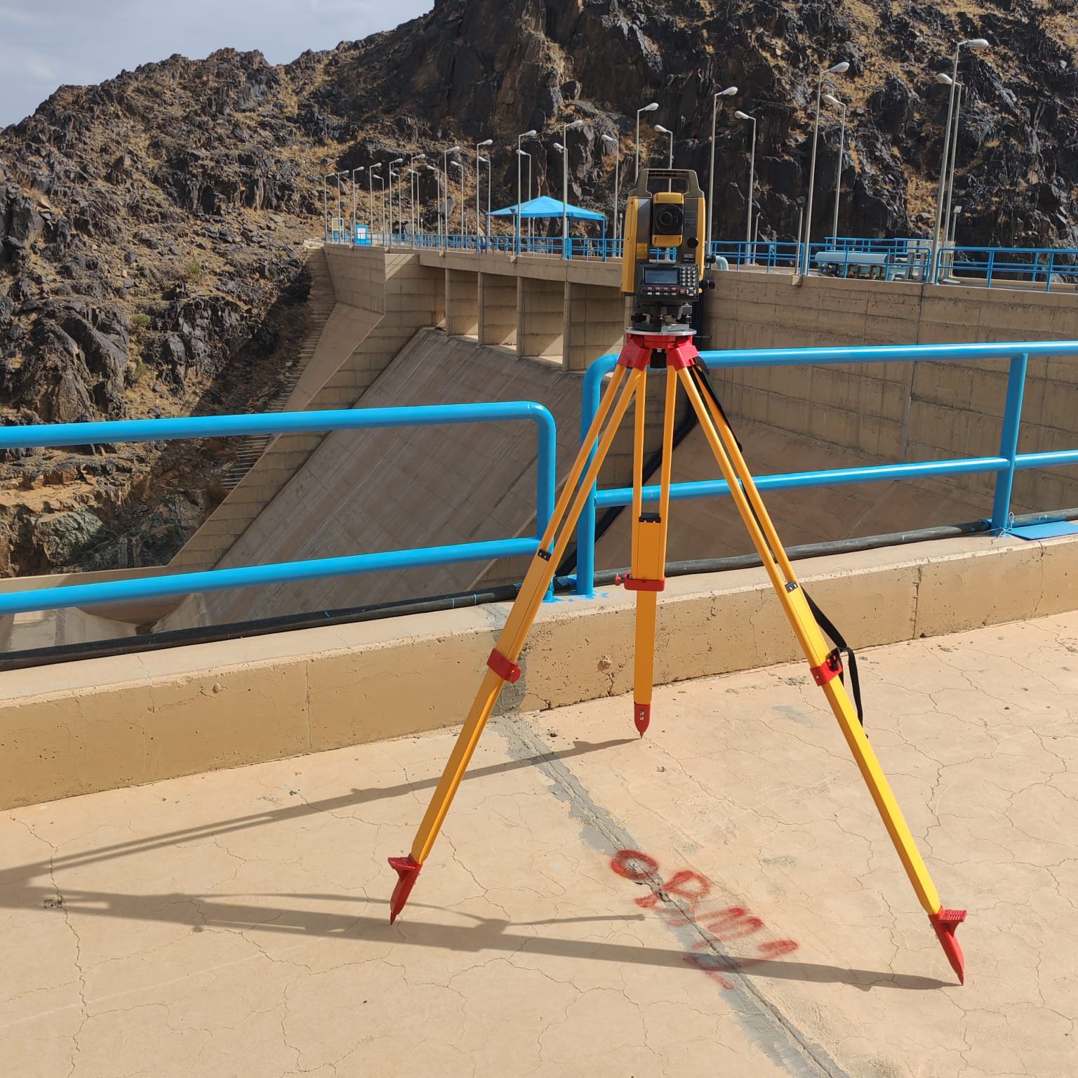 جهاز Total Station مثبت على حامل ثلاثي أمام منشأة سد خرسانية
