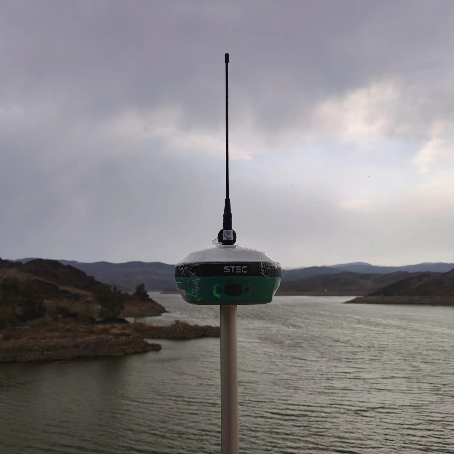 لقطة مقربة لجهاز استقبال مساحي STEC GNSS أمام بحيرة وتضاريس جبلية