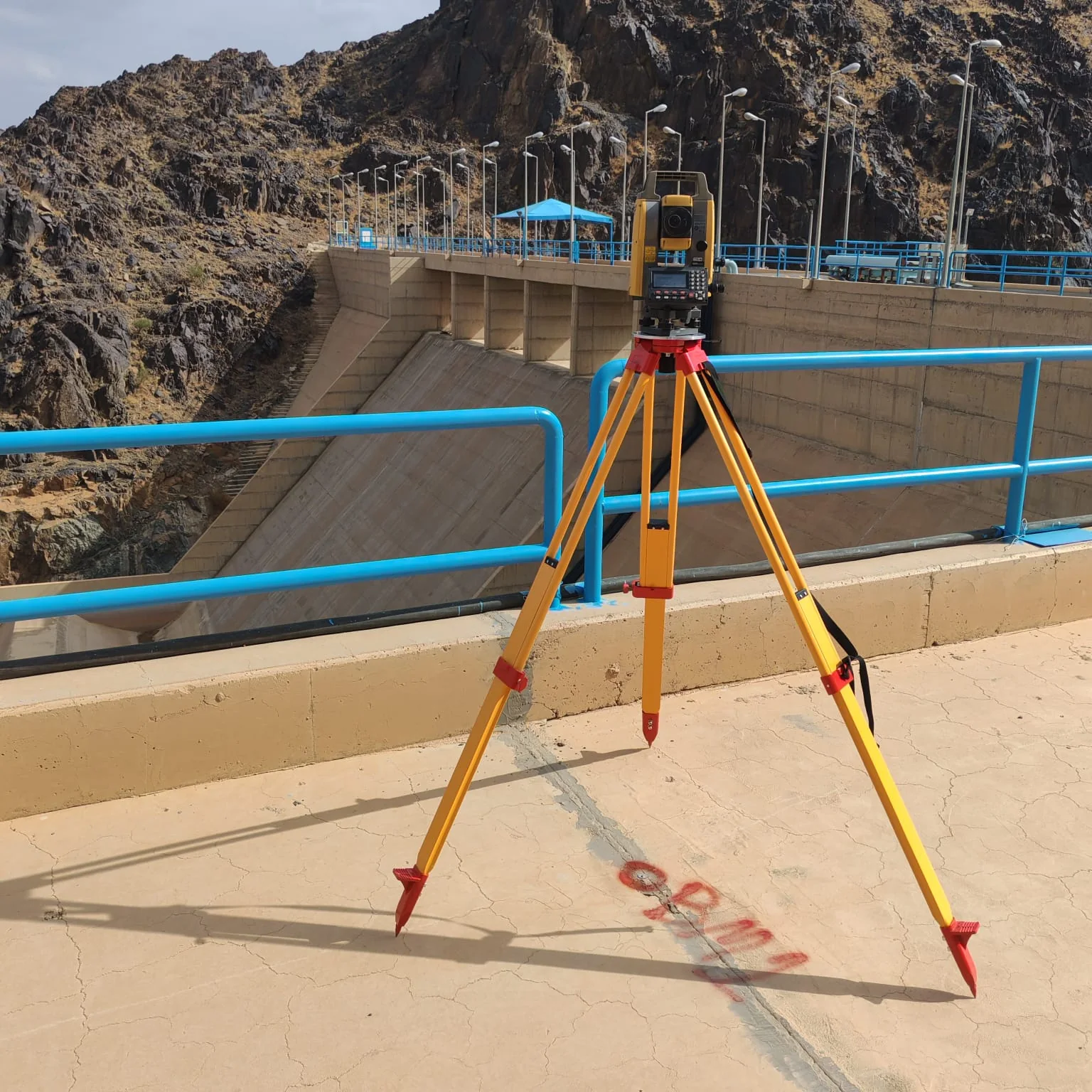 جهاز Total Station مثبت على حامل ثلاثي أمام منشأة سد خرسانية